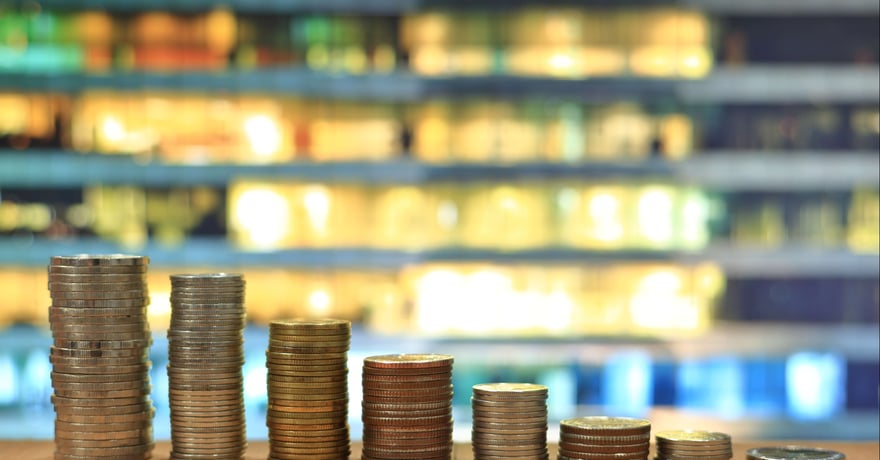 Declining stacks of coins in front of a modern building symbolizing property depreciation.
