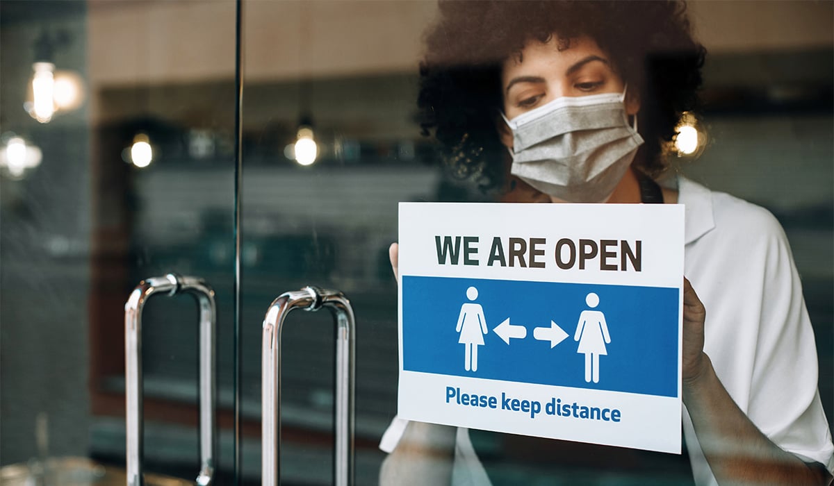 Woman wearing face mask and opening shop with social distancing
