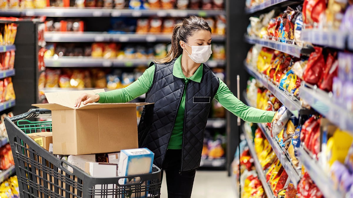 Masked grocery store employee stocks shelves