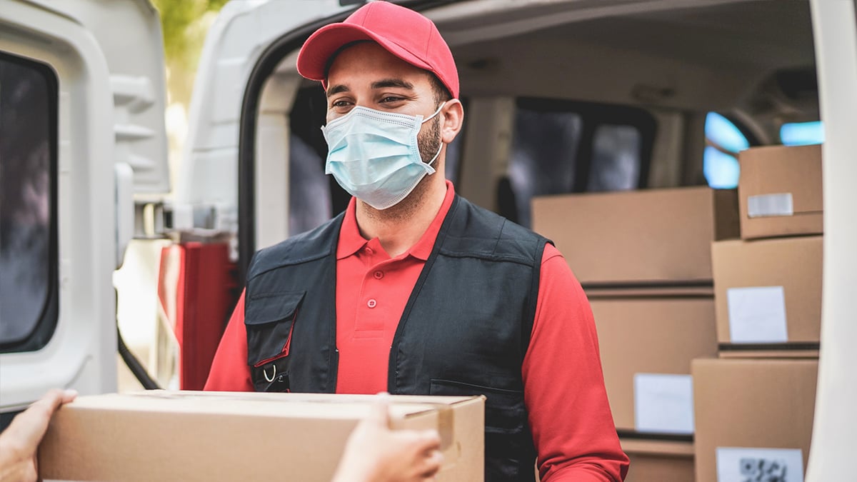 Masked employee handing off cardboard box from truck