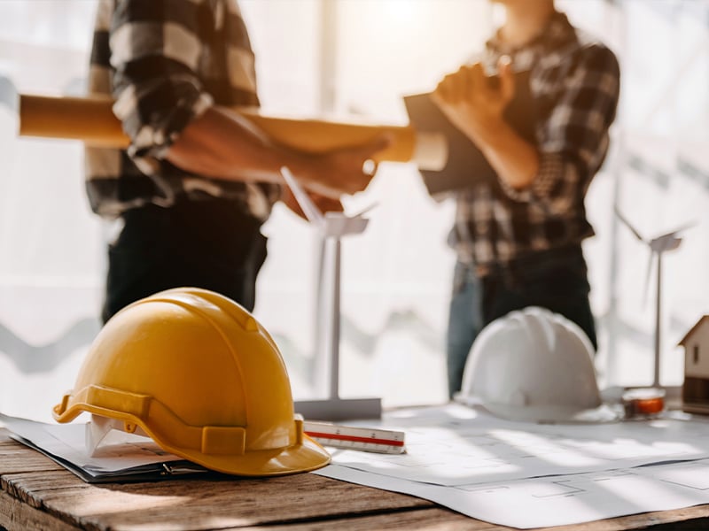 Hard hats on planning table in foreground with architects in background